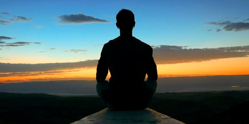 Hombre sentado meditando sobre valle - Médico y coach